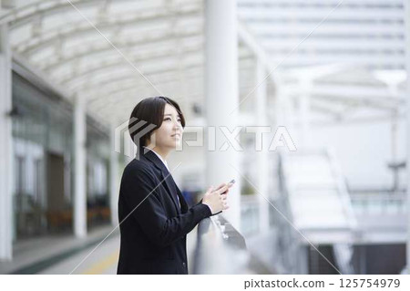 A businesswoman uses her smartphone on a pedestrian overpass in an office district. 125754979