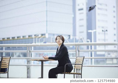 A businesswoman gazing up at the sky from a seat on an outdoor terrace. A businesswoman gazing up at the sky from a seat on an outdoor terrace. 125754980