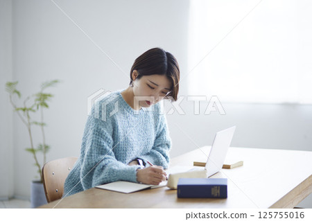 A female university student studying at home while taking notes. A female university student studying at home while taking notes. 125755016