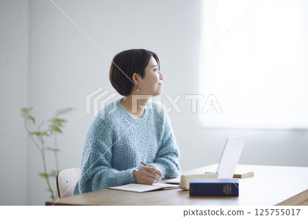 一位女大學生面帶微笑，望著窗外，面前放著筆記本。 125755017