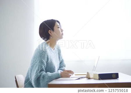 A female university student's profile as she looks up at the window while studying at home. A female university student's profile as she looks up at the window while studying at home. 125755018