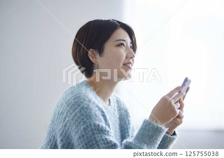 A woman smiling in her room at home, holding her smartphone. 125755038
