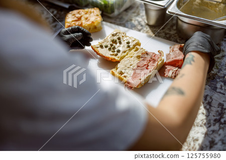 The meticulous preparation of artisan sandwiches takes place within a vibrant culinary setting 125755980
