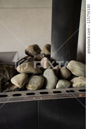 Smooth and rough sauna stones stacked in a metal heater close-up 125756180