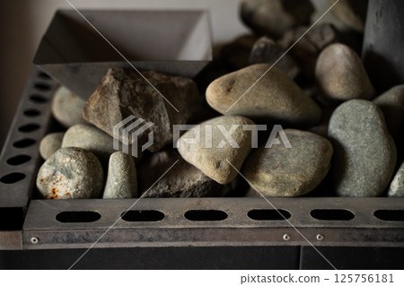 Smooth and rough sauna stones stacked in a metal heater close-up 125756181