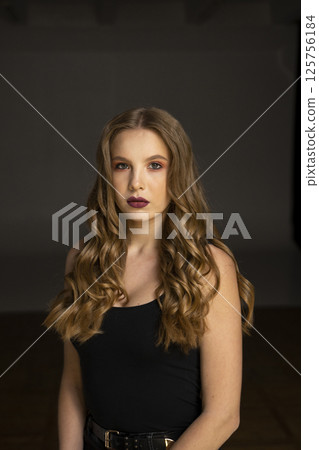 Attractive young woman with long curly hair posing in black top on dark background 125756184