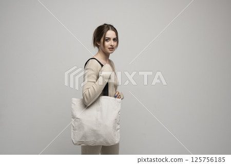 Young woman in beige outfit holding eco tote bag against neutral background Young woman in beige outfit holding eco tote bag against neutral background 125756185