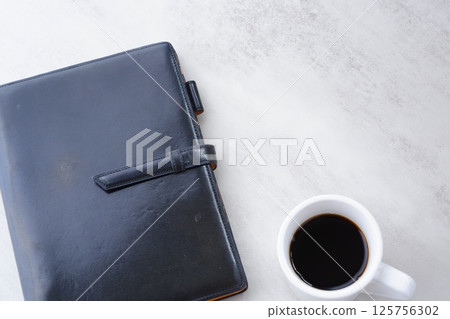 在辦公桌前拿著筆記本一邊喝咖啡一邊工作的圖片 在辦公桌前拿著筆記本一邊喝咖啡一邊工作的圖片 125756302