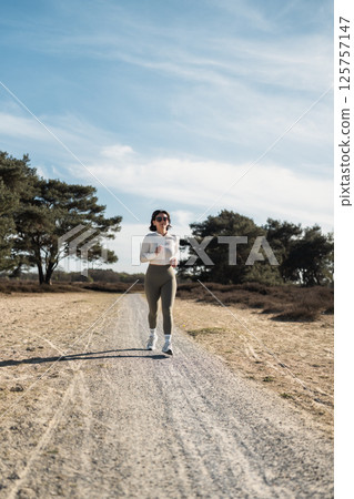 Woman in a white long sleeve shirt runs through soft morning light, blending fitness, mindfulness, and daily routine in a calm outdoor setting Woman in a white long sleeve shirt runs through soft morning light, blending fitness, mindfulness, and daily routine in a calm outdoor setting 125757147