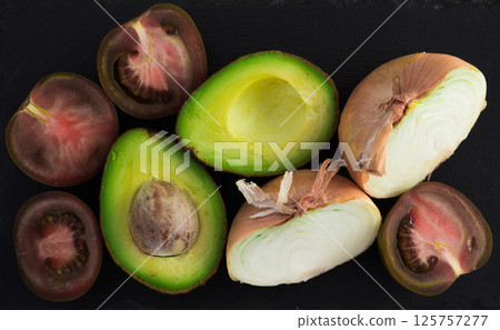 Vegetables black tomatoes, avocado and onions on black stone board 125757277