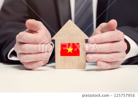 Businessman hand holding wooden home model with Vietnamese flag. insurance and property concepts Businessman hand holding wooden home model with Vietnamese flag. insurance and property concepts 125757958