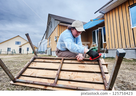 Cleaning bench base with steel brush, skilled DIYer methodically works along metal slats, feeling satisfaction as original shine gradually returns. 125758423
