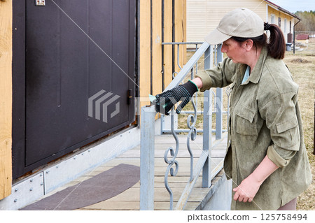 Sanding metal porch railing, practical property caretaker uses abrasive paper to remove rust and dirt, focusing on preparing surface for painting. Sanding metal porch railing, practical property caretaker uses abrasive paper to remove rust and dirt, focusing on preparing surface for painting. 125758494
