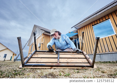 Restoring metal frame of wooden bench, practical garden hobbyist uses paintbrush to apply thick protective coating, concentrating on every exposed joint. Restoring metal frame of wooden bench, practical garden hobbyist uses paintbrush to apply thick protective coating, concentrating on every exposed joint. 125758512