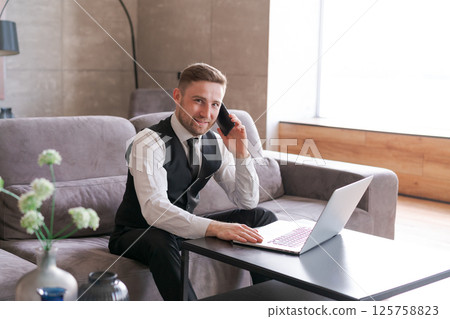 Man is sitting on a couch and talking on a cell phone 125758823