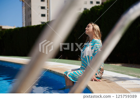 Serene Woman Relaxing by a Swimming Pool on a Sunny Day Serene Woman Relaxing by a Swimming Pool on a Sunny Day 125759389