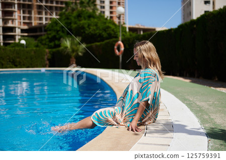 Woman Relaxing by a Swimming Pool on a Bright Sunny Day Woman Relaxing by a Swimming Pool on a Bright Sunny Day 125759391