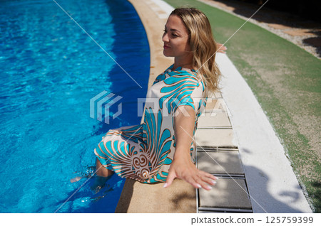 Woman Relaxing at the Edge of a Blue Swimming Pool Outdoors Woman Relaxing at the Edge of a Blue Swimming Pool Outdoors 125759399
