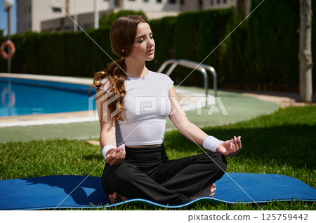 Young Woman Meditating Outdoors Near a Swimming Pool on a Sunny Day 125759442