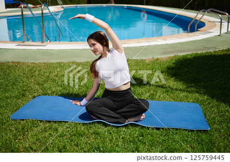 Woman Practicing Yoga Outdoors by a Swimming Pool on a Sunny Day Woman Practicing Yoga Outdoors by a Swimming Pool on a Sunny Day 125759445