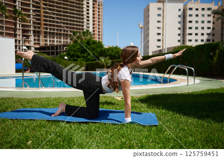 Woman Practicing Yoga Pose Outdoors Near Pool in Urban Setting 125759451