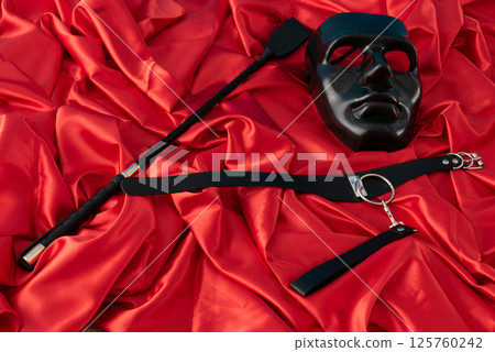 Adult sex games. Kinky lifestyle. Mask and whip ridding crop on the red linen. Bdsm outfit 125760242