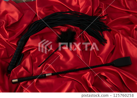 Adult sex games. Kinky lifestyle. Spank and whip ridding crop on the red linen. Bdsm outfit 125760258