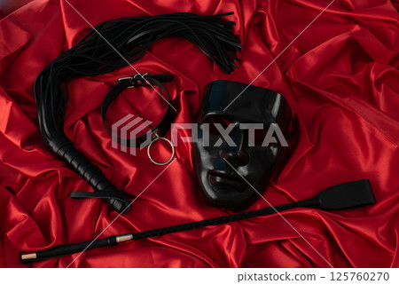 Adult sex games. Kinky lifestyle. Mask and whip ridding crop on the red linen. Bdsm outfit 125760270