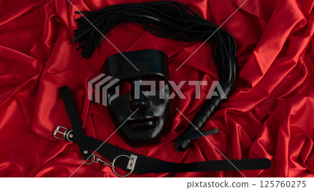 Adult sex games. Kinky lifestyle. Mask and whip ridding crop on the red linen. Bdsm outfit 125760275