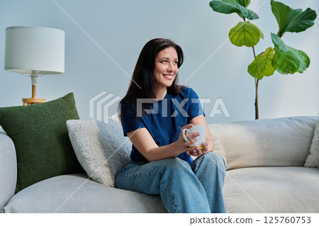 Portrait of beautiful smiling young brunette woman sitting on sofa in living room 125760753