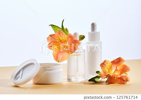 Two serums and a cream in a jar with lily flowers on a beige background. 125761714