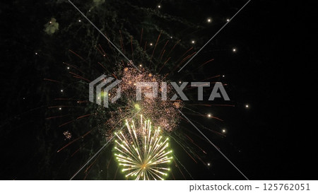 Fireworks magic creates shimmering trace ornaments in black night sky. Spellful firework explosions on display color dark sky. Firework show with glowing patterns in evening sky at holiday party 125762051