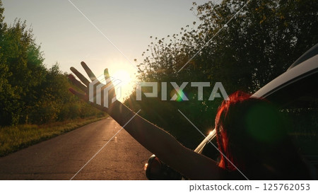 Road trip happy redhead woman with raising hand enjoy freedom fresh air bright sun riding car window closeup back view. Active lifestyle female waving arm travel automobile vehicle journey adventure 125762053