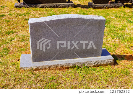 Gray granite tombstone stands alone in peaceful cemetery, illuminated by bright midday sunlight on lush grass. Gray granite tombstone stands alone in peaceful cemetery, illuminated by bright midday sunlight on lush grass. 125762852