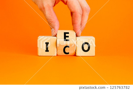 Initial coin or exchange offering symbol. Concept words abbreviation ICO or IEO on wooden block. Beautiful orange background. Business Initial coin or exchange offering concept. Copy space. 125763782