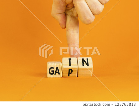 Gain or gap symbol. Concept words Gain Gap on wooden block. Beautiful orange table orange background. Businessman hand. Business gain or gap concept. Copy space. Gain or gap symbol. Concept words Gain Gap on wooden block. Beautiful orange table orange background. Businessman hand. Business gain or gap concept. Copy space. 125763818
