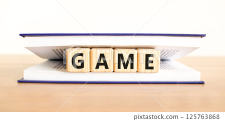 Game symbol. Concept word Game on beautiful wooden blocks in book. Beautiful wooden table white background. Business, lifestyle and game concept. Copy space. Game symbol. Concept word Game on beautiful wooden blocks in book. Beautiful wooden table white background. Business, lifestyle and game concept. Copy space. 125763868