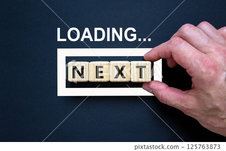 Next symbol. Concept word Loading Next on beautiful wooden blocks. Businessman hand. Beautiful black table black background. Business, lifestyle, support and next concept. Copy space. 125763873
