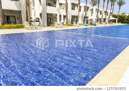 Summer seaside relax mood travel vacation a luxurious pool hotel interior for a summer holiday in warm countries. Beautiful tropical beach hotel resort with swimming pool, sun loungers palm trees 125763955