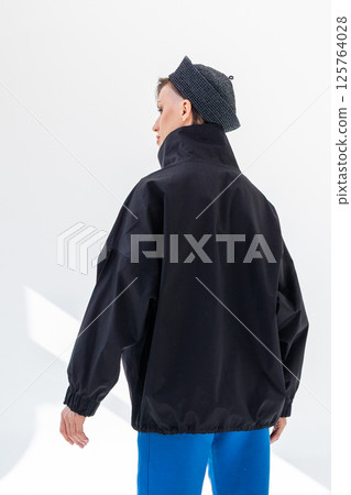 Elegant woman in black windbreaker jacket, blue pants and nautical hat on white background. Fashionable female in ocean French style. tudio photography. Vertical photo. High quality photo Elegant woman in black windbreaker jacket, blue pants and nautical hat on white background. Fashionable female in ocean French style. tudio photography. Vertical photo. High quality photo 125764028