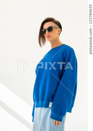 Elegant woman in blue sweatshirt and light blue skirt on white background. Fashionable female style. Studio photography. Vertical photo. High quality photo 125764035