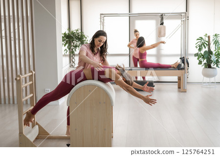 A trainer adjusts woman on a Ladder Barrel. A trainer adjusts woman on a Ladder Barrel. 125764251