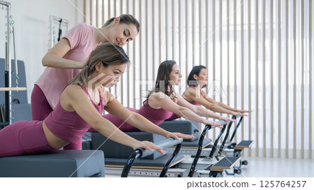 A trainer adjusts women on a reformer. 125764257