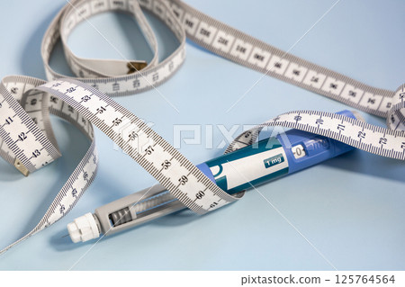 Ozempic syringe pen and measuring tape on blue Ozempic syringe pen and measuring tape on blue 125764564