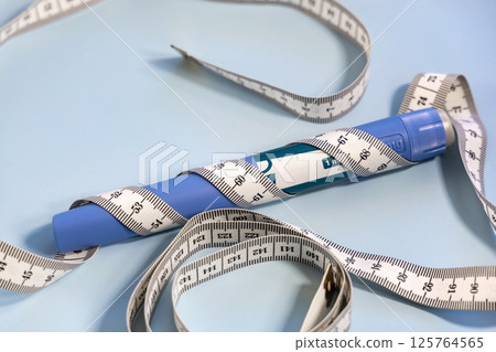 Ozempic syringe pen and measuring tape on blue Ozempic syringe pen and measuring tape on blue 125764565