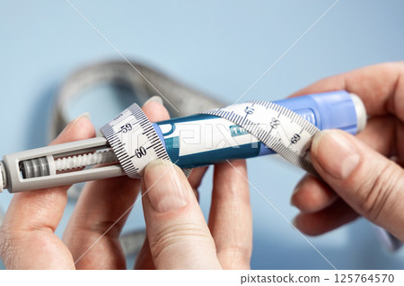 Female hands holding Ozempic syringe pen and measuring tape on blue Female hands holding Ozempic syringe pen and measuring tape on blue 125764570