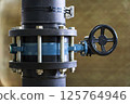 Detailed Close-up of a Black Industrial Pipe with a Blue Flanged Valve and Handwheel for Manual Flow Control 125764946