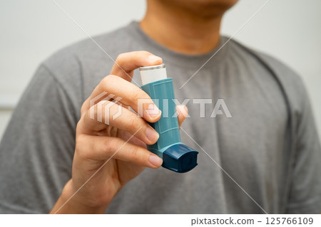 Asthma and chronic obstructive pulmonary disease COPD, Asian young man using metered dose inhaler MDI. 125766109