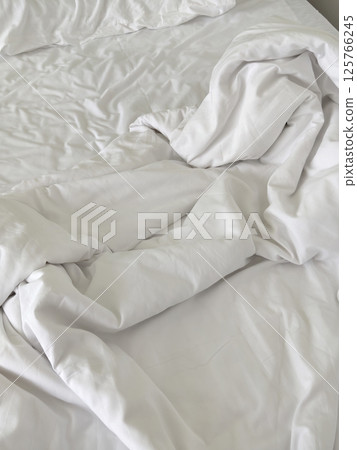 Wrinkled bed sheets and blanket on a bed. 125766245