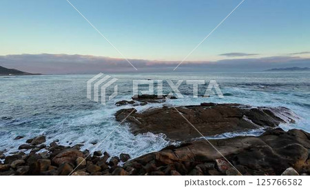 A Tranquil and Serene Coastal View at Sunset, Featuring Gentle Waves and Rocky Outcroppings 125766582